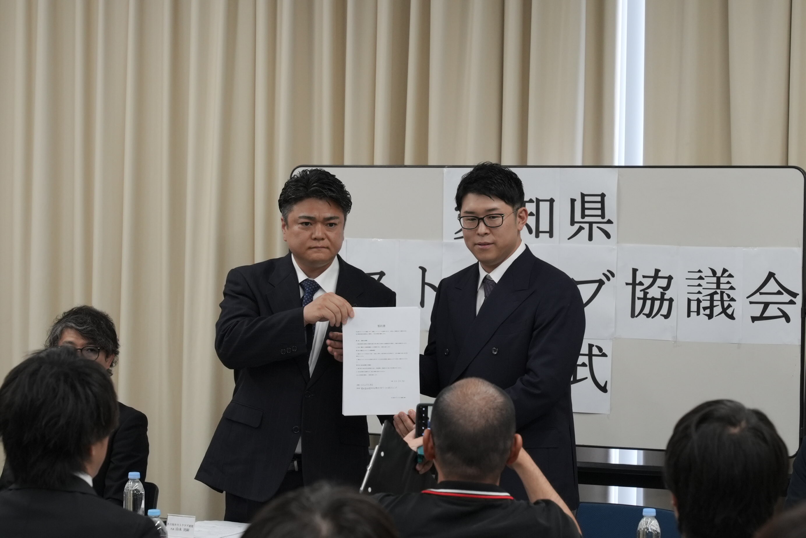 協議会の発足式で書面を掲げる2人と会場の様子